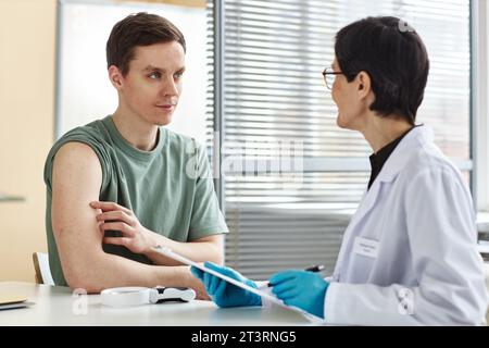 Porträt eines lächelnden jungen Mannes, der sich mit einer Ärztin in der Klinik berät und auf die Schulter zeigt Stockfoto