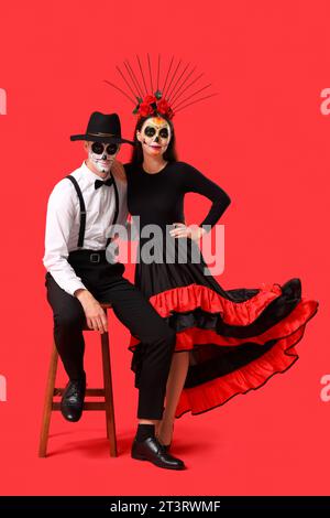 Junges Paar, das für Mexikos Tag der Toten (El Dia de Muertos) auf rotem Hintergrund gekleidet ist Stockfoto