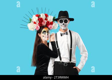 Junges Paar, das für Mexikos Tag der Toten (El Dia de Muertos) auf blauem Hintergrund gekleidet ist Stockfoto