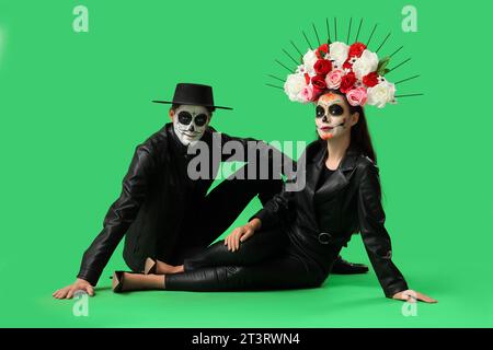 Junges Paar, das für Mexikos Tag der Toten (El Dia de Muertos) auf grünem Hintergrund gekleidet ist Stockfoto