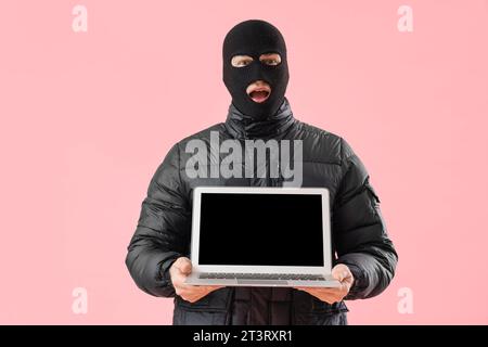 Junger Mann in Winterkleidung mit Laptop auf rosa Hintergrund Stockfoto