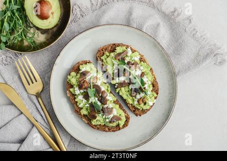 Avocadotoast mit Pilzen, Feta und Mikrogrün auf Vollkornbrot, Blick von oben. Vegetarische Speisen. Veganes Menü. Stockfoto