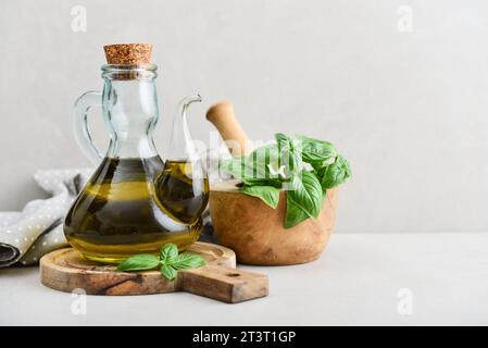 Olivenöl in Vintage-Flasche mit Basilikum und hölzernem Schneidebrett auf hellem Hintergrund Stockfoto