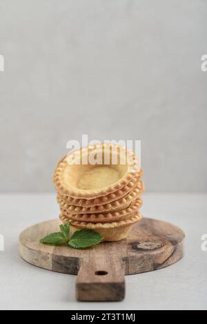 Leere Tartlet-Schalen auf hölzernem Schneidebrett auf hellem Hintergrund Stockfoto