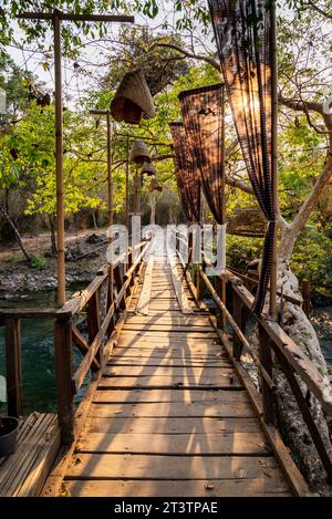Bei Sonnenuntergang. Das Sonnenlicht scheint durch eine Holzkonstruktion einer schmalen Fußgängerbrücke, die zu den wichtigsten Wasserfällen und Stromschnellen der Insel Don Khon führt. Stockfoto