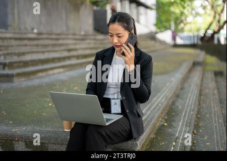 Eine beschäftigte, professionelle und konzentrierte Millennials-asiatische Geschäftsfrau in einem formellen Business-Anzug spricht mit ihrem Kunden, während sie arbeitet Stockfoto