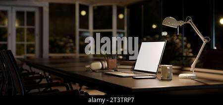 Seitenansicht eines Laptop-Modells mit weißem Bildschirm, einer Tischlampe und Accessoires auf einem Besprechungstisch in einem modernen Tagungsraum bei Nacht. Dunkler Arbeitsbereich Co Stockfoto