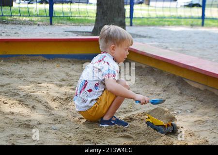 Niedlicher Kleinkinder, der im Sand auf dem Spielplatz im Freien spielt. Wunderschönes Baby, das Spaß an sonnigen warmen Sommertagen hat. Hochwertige Fotos Stockfoto