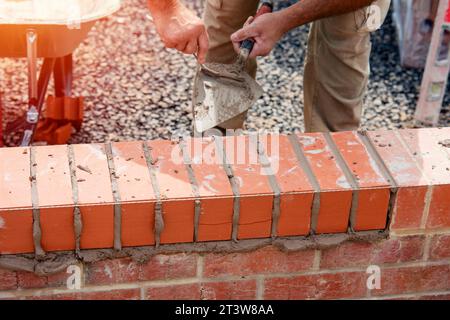 Nahaufnahme einer Mauer aus Ziegelstein und einer Kelle, die der Arbeiter zum Auftragen und Glätten des Mörtels zwischen Ziegelsteinen verwendet. Maurer, der den letzten Schliff auf den Ziegelstein legt Stockfoto