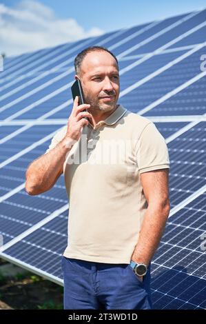 Selbstbewusster Geschäftsmann, der einen wichtigen Anruf hat. Ein Mann, der über seine Investition in alternative Energiequellen spricht. Mann, der auf dem Hintergrund von Solarpaneelen telefoniert. Stockfoto