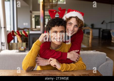 Porträt eines glücklichen, vielseitigen schwulen Paares, das weihnachtsmützen trägt und zu Hause Videoanrufe macht Stockfoto