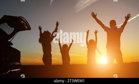 Glückliche Familie hebt bei Sonnenuntergang die Hände in der Nähe des Fahrzeugs Stockfoto