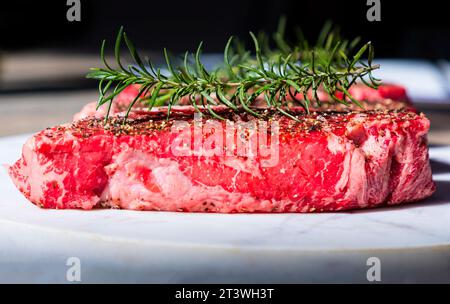 Rohes Wagyu-Steak mit Rosmarinzweig im Freien auf einem weißen Teller Stockfoto