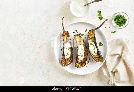 Im Ofen geröstete Aubergine mit Knoblauch-Joghurt-Dressing auf Teller über hellem Steinhintergrund mit Kopierraum. Draufsicht, flach Stockfoto