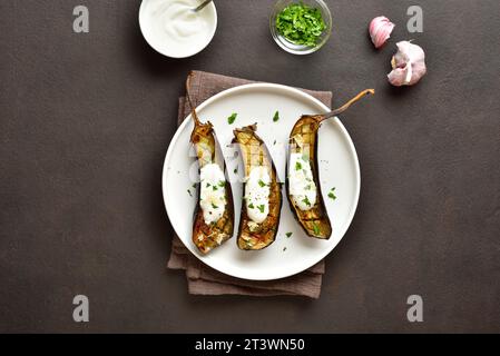 Gebackene Aubergine mit Knoblauch-Joghurt-Dressing auf Teller auf dunklem Hintergrund. Draufsicht, flach Stockfoto