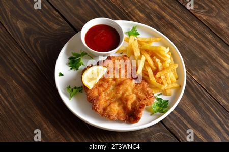 Hausgemachtes paniertes Schnitzel mit Kartoffelfritten und Sauce auf weißem Teller über Holztisch. Nahaufnahme der Vuew Stockfoto