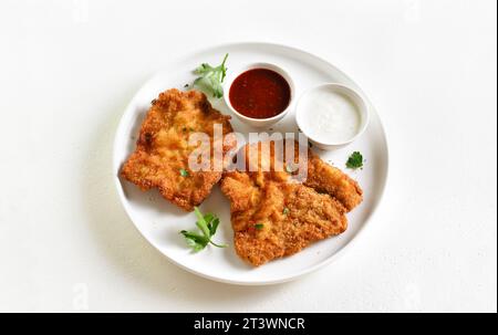 Paniertes wiener Schnitzel mit Sauce auf Teller auf weißem Hintergrund. Nahansicht Stockfoto