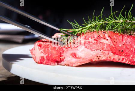 Rohes Wagyu-Steak mit Rosmarinzweig im Freien auf einem weißen Teller Stockfoto