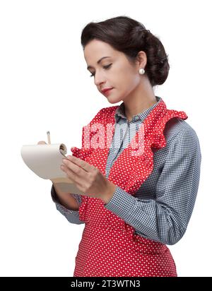 Lächeln auf den Lippen Vintage Hausfrau ein Rezept Zutaten auf einem Notizblock aufschreiben Stockfoto
