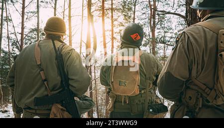 Rückansicht auf Reenactors gekleidet als American Infantry Soldier Watch for Bright Sun at Winter Day. Gruppe Von Us-Soldaten Bewaffnet Von Sturmgewehr 44 Or Stockfoto