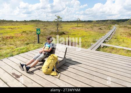 Touristenwanderer entspannen auf einer Holzbank im Kakerdaja Moor, Wanderweg umgeben von kleinen Teichen an einem schönen sonnigen Sommertag in Estland Stockfoto