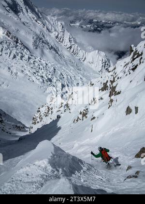 Ein Skifahrer fährt in den Bergen ein Couloir hinunter. Stockfoto