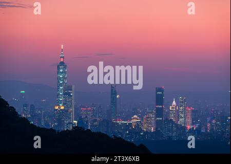 Nach und nach leuchten bunte Lichter am Abend auf. Orange-rote Nachtansicht auf die Stadt nach Sonnenuntergang im Herbst. Taipeh, Taiwan. Stockfoto