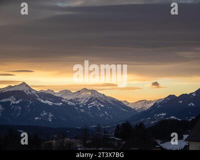 Farbenfroher Winterschneeuntergang über einem österreichischen alpendorf mit Bergen im Hintergrund, schneebedeckten Dächern, Kärnten, Österreich Stockfoto