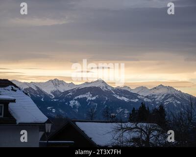 Farbenfroher Winterschneeuntergang über einem österreichischen alpendorf mit Bergen im Hintergrund, schneebedeckten Dächern, Kärnten, Österreich Stockfoto