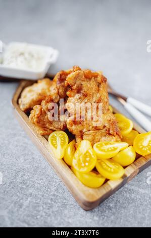 Das Fischgericht besteht aus gebratenem Kabeljaufilet mit einer cremigen Sauce und gelben Pflaumentomaten, serviert auf einer fischförmigen Holzplatte. Stockfoto
