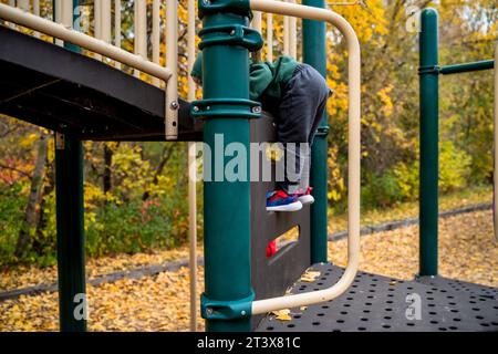 Kleinkind klettert am kühlen Herbsttag die Stufen des Spielplatzes hinauf Stockfoto