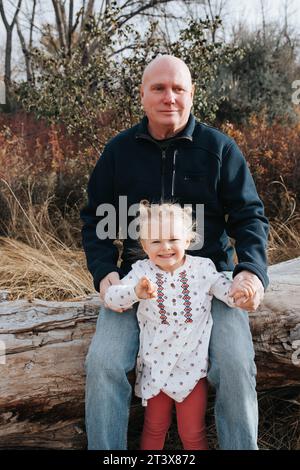 Opa und die vierjährige Enkelin sitzen auf einem Herbststamm. Stockfoto