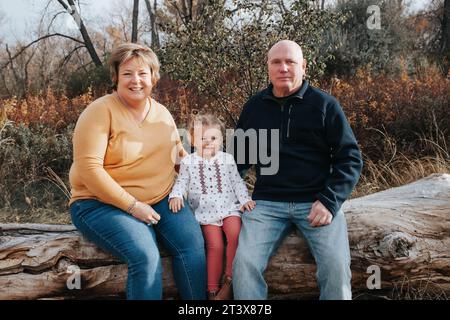 Großeltern und vierjährige Enkelin auf einem Herbststamm Stockfoto