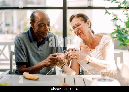 Seniorin, die männlichen Freunden Häkeln im Pflegeheim beibringt Stockfoto