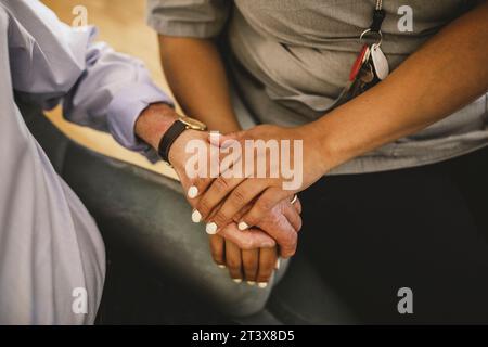 Mittelteil einer jungen Krankenschwesterin, die Hände hält, während sie einen Seniorenmann im Altersheim tröstet Stockfoto