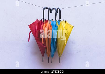 Bunte Regenschirme hängen an einer Wäscheleine an einer weißen Wand Stockfoto