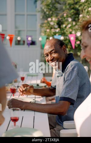 Porträt eines lächelnden älteren Mannes, der mit einer Frau am Esstisch im Hinterhof sitzt Stockfoto