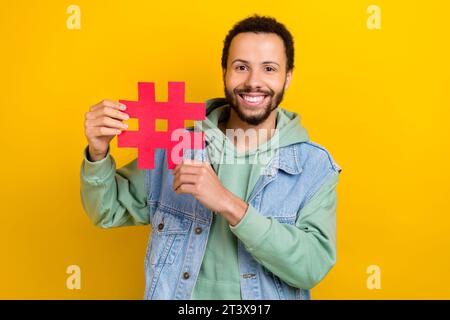 Foto-Porträt des attraktiven jungen Mannes Hashtag Zeichen Influencer gekleidet stilvolle Khaki Kleid isoliert auf gelbem Farbhintergrund Stockfoto