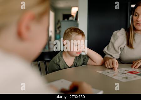 Junge mit Down-Syndrom, der bei der Mutter sitzt und zu Hause unterrichtet Stockfoto