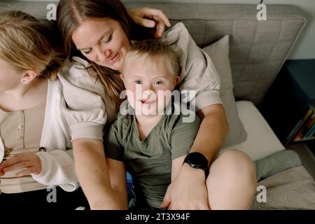 Hochwinkelporträt eines Jungen, der mit Familie zu Hause auf dem Bett sitzt Stockfoto