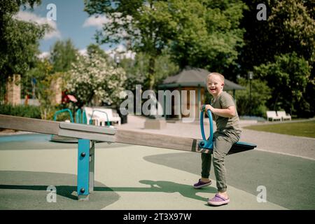 Seitliches Langformat-Porträt von Happy Boy mit Down-Syndrom, das Wippe im Park genießt Stockfoto
