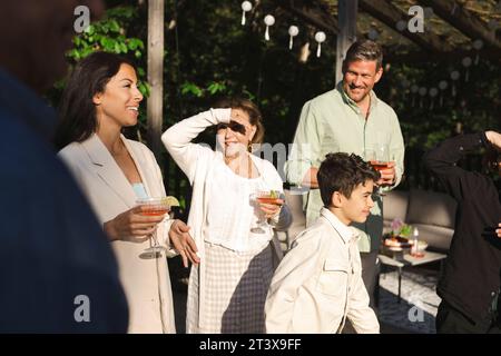 Ältere Frau, die Augen abschirmt, während sie bei der Familie auf der Terrasse im Hinterhof steht Stockfoto