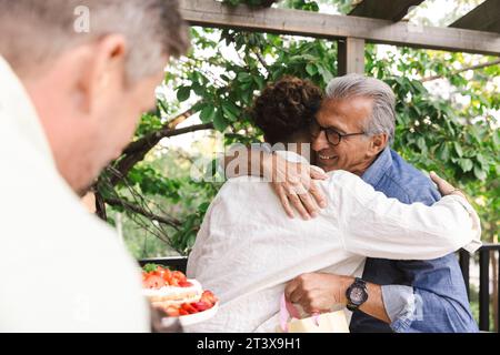Glücklicher Senior-Mann, der den jungen Mann auf der Dinnerparty umarmt Stockfoto