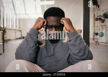 Trauriger junger Geschäftsmann sitzt mit Kopf in Händen im Büro Stockfoto