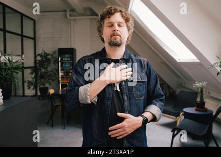 Geschäftsmann mit geschlossenen Augen und Hand auf Brust im Büro Stockfoto