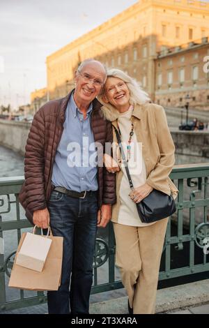 Porträt eines glücklichen Seniorenpaares, das in der Stadt auf einem Geländer sitzt Stockfoto