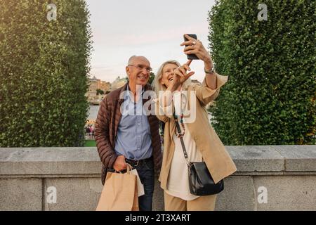 Glückliche Seniorin, die Selfie mit einem Mann macht, der auf Geländer lehnt Stockfoto