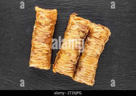 Drei Stücke süßer Baklava auf Schieferstein, Makro, Draufsicht. Stockfoto