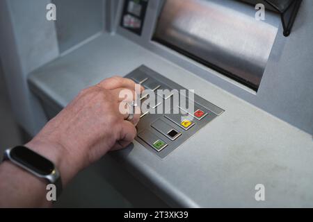 Frau mittleren Alters, die den Geldautomaten benutzt und die PIN-Sicherheit auf dem Nummernblock drückt. Stockfoto