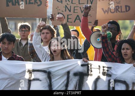 Eine Gruppe von Aktivisten, die Banner und Schilder halten und sich leidenschaftlich für Veränderung und Gerechtigkeit einsetzen, mit einer jungen Frau, die den Gesang anführt, und einem weiteren u Stockfoto